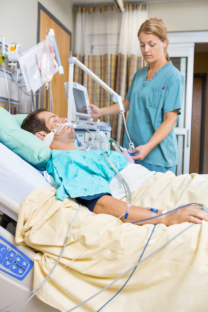 Pflegefachfrau überprüft den Zustand eines Patienten, der im Krankenbett liegt, und bedient einen Überwachungsmonitor